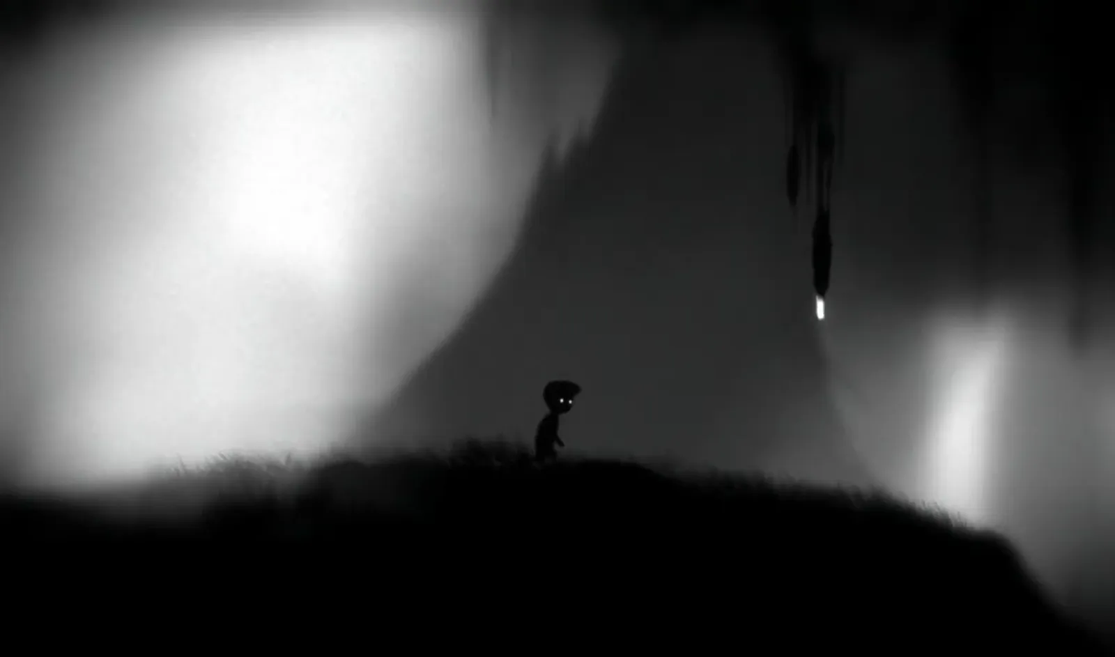 LIMBO's monochrome world, the silhouetted boy standing on a grassy ledge in a foggy cavern